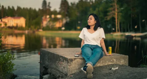 LUT University master's student sitting on a concrete block at the shore