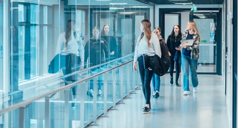 Kolme opiskelijaa kävelee yliopiston käytävällä.