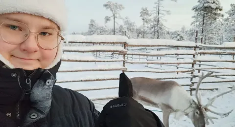 Veeti is showing a thumbs up in front of a reindeer. 