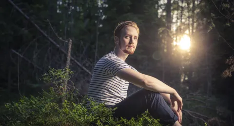 Henkilö istuu metsässä ja aurinko paistaa.