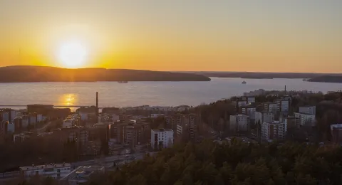 Kaupunkimaisema illalla. Kerrostaloja, metsää ja järvi.
