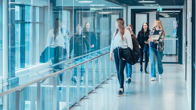 Kolme opiskelijaa kävelee yliopiston käytävällä.