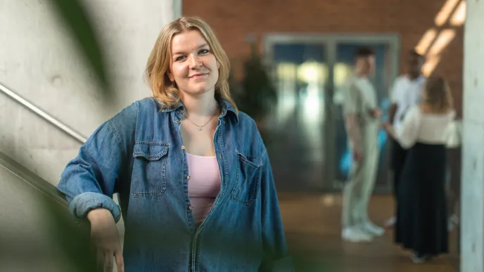 Opiskelijoita kauppakorkeakoulun tiloissa, joista yksi katsoo kameraan ja hymyilee.