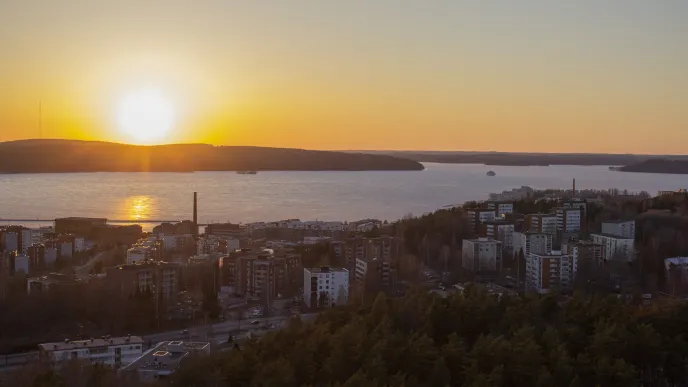 Kaupunkimaisema illalla. Kerrostaloja, metsää ja järvi.