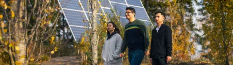 Kansainvälisiä opiskelijoita kävelemässä aurinkopaneelien ohi.