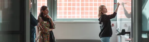 Henkilö kirjoittaa fläppitaululle ja toinen katsoo.