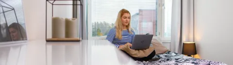 Opiskelija istuu sängyllä tietokone sylissä