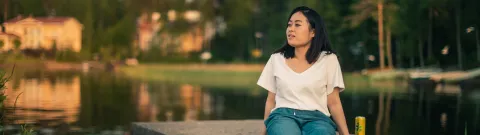 Opiskelija istuu veden äärellä ja katselee maisemia.