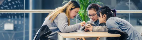 Opiskelijoita pöydän ääressä katsomassa puhelinta.
