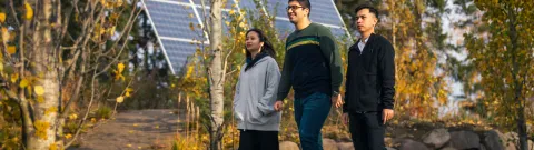 Opiskelijoita kävelemässä yliopiston pihalla. Taustalla näkyy aurinkopaneeli.