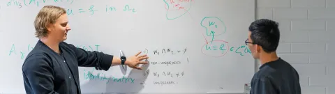 Laskennallisen tekniikan harjoitus, jossa kaksi ihmistä katsoo merkintöjä valkotaulussa.