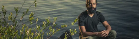 Henkilö istuu veden äärellä.